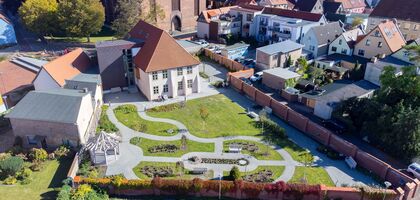 Luftaufnahme: Zeigt das ganz Grundstück des Papenhofs, das Gebüde und den Garten mit schlängelnden Gartenwegen, umringt von einer Mauer und der Altstadt, im hintergrund der untere Teil der Sankt Marien Kirche
