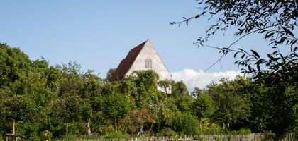 Altes Land-Kirchengebäude in einem Obstbaumgarten. Davor ein Holzzaun. Im Vordergrun eine Wiese.